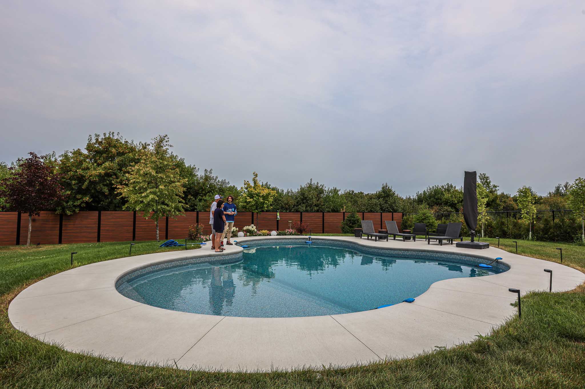 Vinyl inground swimming pool with curved design installed by HB Pools in Greely, Ontario, featuring a spacious backyard and HB Pools technician consulting homeowners on pool maintenance.