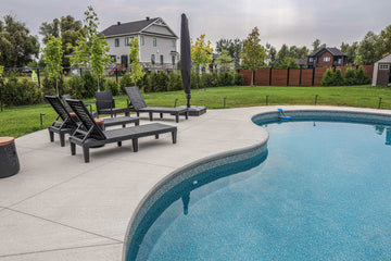 Spacious vinyl inground swimming pool patio with modern lounge chairs and umbrella installed by HB Pools in Greely, Ontario, featuring a smooth concrete deck and landscaped backyard.