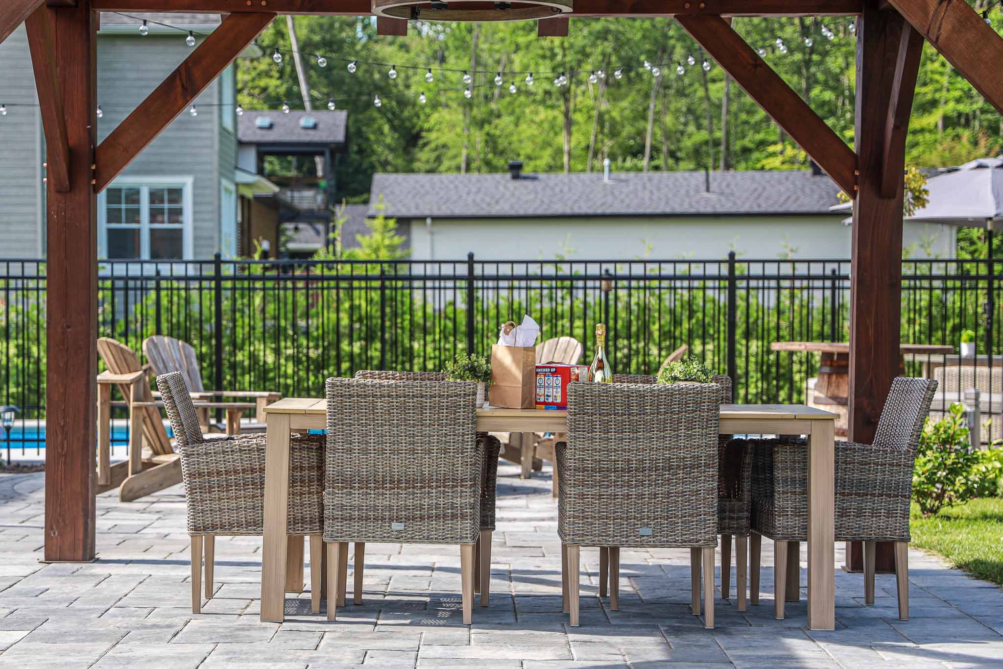 Outdoor dining area with wicker chairs and wooden table under a pergola beside a vinyl inground pool, installed by HB Pools in Navan, Ontario, featuring stone patio and landscaped backyard.