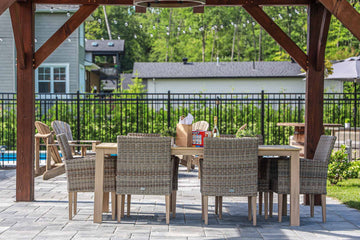 Outdoor dining area with wicker chairs and wooden table under a pergola beside a vinyl inground pool, installed by HB Pools in Navan, Ontario, featuring stone patio and landscaped backyard.