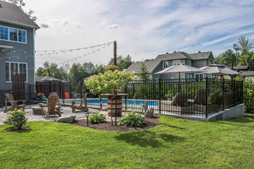 Vinyl inground swimming pool with black metal fencing and outdoor patio featuring lounge chairs and firepit, installed by HB Pools in Navan, Ontario, surrounded by landscaped yard and residential homes.