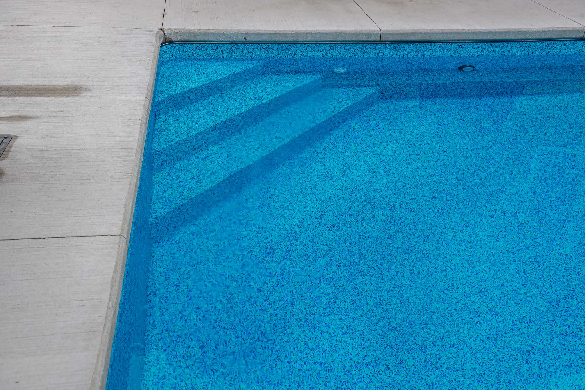 Close-up of vinyl inground pool steps with blue patterned liner and clean concrete bullnose coping, installed by HB Pools in Rockland, Ontario."