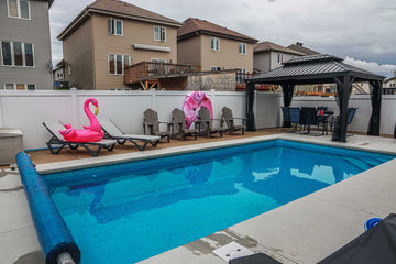 Rectangular vinyl inground swimming pool with wood composite decking, Adirondack chairs, a pink flamingo float, and a gazebo with outdoor dining furniture, installed by HB Pools in Rockland, Ontario.