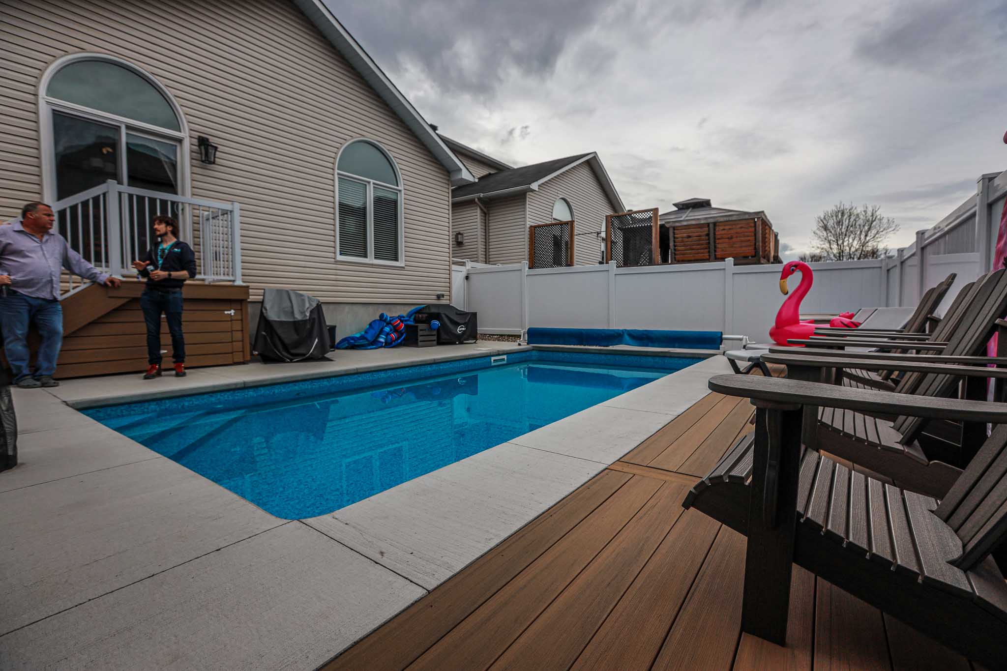 Rectangular vinyl inground swimming pool with concrete and wood decking, surrounded by privacy fencing and lounge chairs, installed by HB Pools in Rockland, Ontario.