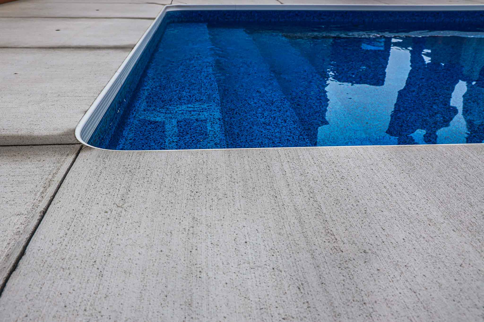 Close-up of vinyl inground pool steps with textured concrete coping, installed by HB Pools in Orleans, Ontario, showcasing clean edges and durable pool liner.