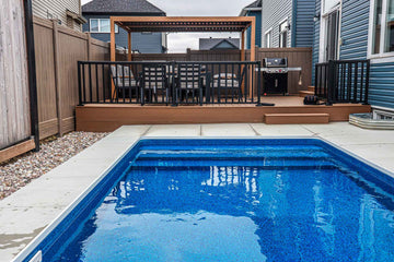 Rectangular vinyl inground swimming pool with built-in steps, surrounded by clean concrete coping and adjacent to a raised wood deck with outdoor dining furniture, installed by HB Pools in Orleans, Ontario.