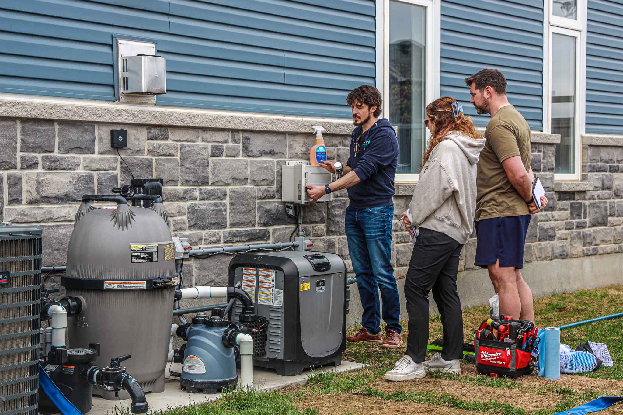 HB Pools technician demonstrating pool filtration and heating equipment to homeowners in Orleans, Ontario, highlighting expert pool maintenance and care services.