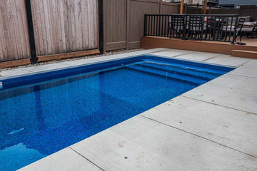 Rectangular vinyl inground swimming pool with built-in steps and surrounding concrete coping, adjacent to a raised wood deck, installed by HB Pools in Orleans, Ontario.