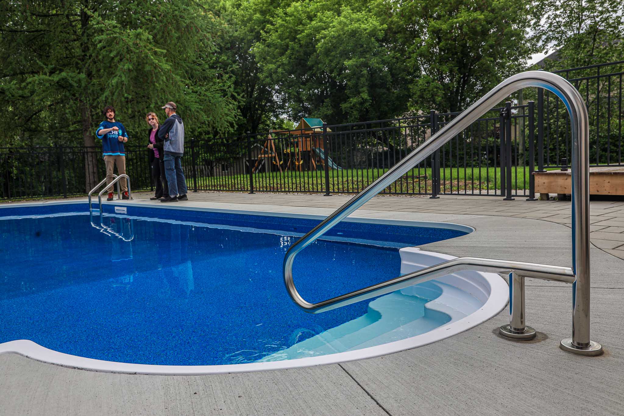 Vinyl inground swimming pool with stainless steel handrails installed by HB Pools in Limoges, Ontario, featuring a clean pool deck and HB Pools team consulting clients in the backyard.