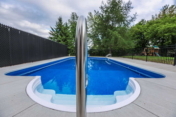 Vinyl inground swimming pool with curved steps and stainless steel handrail installed by HB Pools in Limoges, Ontario, surrounded by a clean concrete deck and privacy fencing.