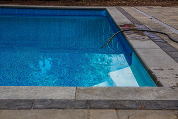 A leak detection services technician is inspecting a residential swimming pool for hidden water leaks using submerged hose equipment.