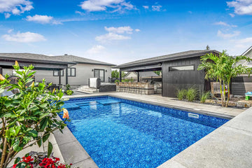 Luxury backyard featuring a rectangular inground pool with a vibrant blue mosaic pattern liner and modern pool house | HB Pools