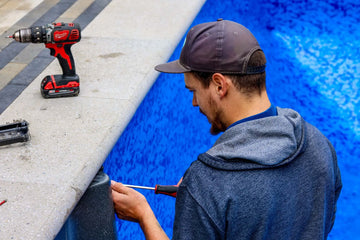 Pool professional using a screwdriver and power drill to secure a new vinyl liner to the pool coping | HB Pools